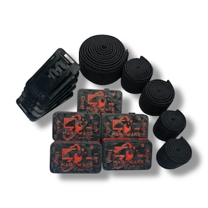 Könnte beinhalten: Eine Auswahl an schwarzer Fitness-Hardware, darunter mehrere Rollen schwarzer elastischer Bänder, mehrere kleine schwarze Boxen mit rotem Text und Grafiken sowie ein Stapel schwarzer Kunststoffclips. Die Boxen sind mit Körperteilnamen beschriftet.