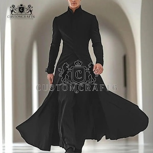 Puede incluir: Un abrigo largo negro con cuello alto y mangas largas. El abrigo tiene un diseño fluido y está hecho de una tela oscura. El texto "CUSTOMCRAFT6" es visible en el abrigo. Es una prenda elegante.