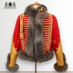 Puede incluir: Chaqueta roja de estilo militar con adornos dorados, botones y borlas. La chaqueta presenta un cuello y puños de piel gris. El logotipo Customcraft6 es visible.