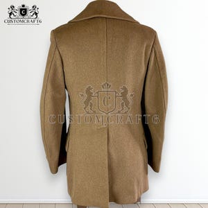 May include: A tan wool coat with a notched lapel and a double-breasted design. The back of the coat features a decorative crest with the text "CUSTOMCRAFT6". The coat is a classic style, suitable for cooler weather.