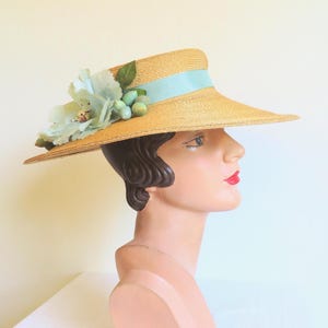 Peut inclure: Un chapeau de paille &agrave; larges bords avec un ruban bleu clair et une fleur en guise d'ornement. Le chapeau est port&eacute; sur la t&ecirc;te d'un mannequin.