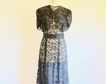 May include: A black lace dress with a matching lace jacket. The dress has a fitted bodice and a full skirt. The jacket has short sleeves and a round neckline.