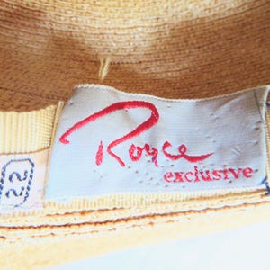 Peut inclure: Un gros plan d'un chapeau de paille jaune avec une &eacute;tiquette blanche sur laquelle est inscrit "Royce Exclusive" en lettres rouges. L'&eacute;tiquette est attach&eacute;e au chapeau avec un ruban jaune.