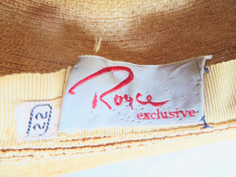 Peut inclure: Un gros plan d'un chapeau de paille jaune avec une &eacute;tiquette blanche sur laquelle est inscrit "Royce Exclusive" en lettres rouges. L'&eacute;tiquette est attach&eacute;e au chapeau avec un ruban jaune.