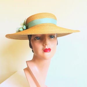 Peut inclure: Un chapeau de paille &agrave; larges bords avec un ruban bleu clair et une fleur en accent. Le chapeau est port&eacute; sur une t&ecirc;te de mannequin.