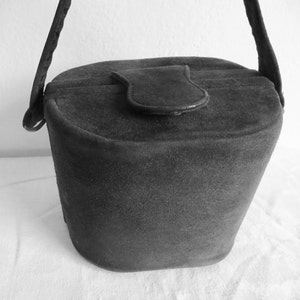 Puede incluir: Un bolso de mano negro estilo cubo con una textura suave y mate. El bolso presenta un cierre de solapa superior redondeado con una leng&uuml;eta central y una sola correa para el hombro unida a los lados. La forma es c&oacute;nica, m&aacute;s ancha arriba.