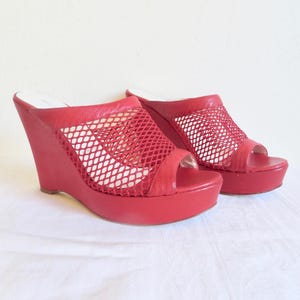 May include: A pair of red wedge sandals with a mesh upper. The sandals have a peep toe and a platform sole.