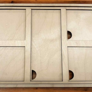 May include: A light-colored wooden organizer with six rectangular compartments. Each compartment has a semi-circular cutout for easy access. The frame is outlined with a thin black border, and the wood grain is visible.