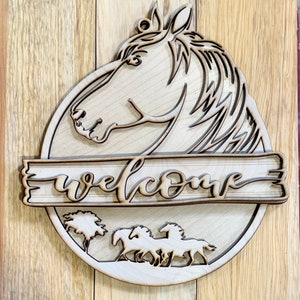 May include: Wooden welcome sign with a horse head cutout, the word "welcome" in a decorative script, and a silhouette of three horses running in a field.