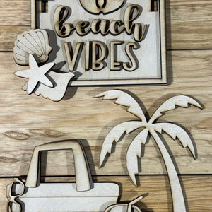 May include: Wooden cutout set with a beach theme. The set includes a sign that says "beach vibes", a palm tree, a beach bag, a coconut with a straw, and two seashells with starfish.