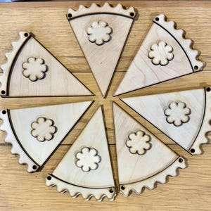 May include: Eight unfinished wooden pennants with scalloped edges and a simple flower design in the center. The pennants are arranged in a circle.