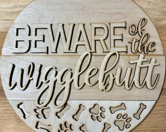 May include: A round wooden sign with the text "BEWARE of the wigglebutt" in a decorative font. The sign is decorated with paw prints and bone shapes.