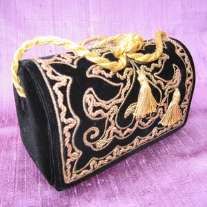 May include: A black velvet handbag with a gold rope handle and gold embroidery. The handbag has two gold tassels.