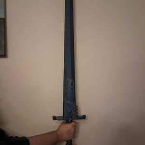 May include: A large, dark grey sword with a long, pointed blade. The hilt features intricate geometric designs and a crossguard. The sword is held by a person. The design suggests a fantasy or historical theme.