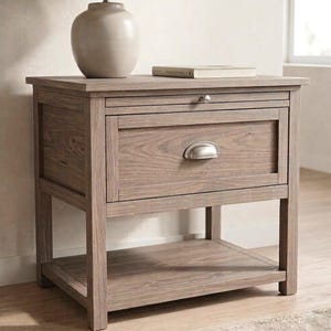 May include: A wooden nightstand with a drawer and a lower shelf. The nightstand is topped with a lamp and a book. The drawer has a metal handle. The wood has a light brown finish.