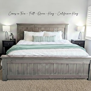May include: A gray wooden bed frame with a matching headboard. The bed is made with white bedding, a green blanket, and decorative pillows. The text on the wall reads "Comes in Twin - Full - Queen - King - California King".