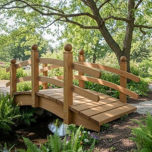 Könnte beinhalten: Eine hellbraune Holzbrücke überspannt einen Bach. Die Brücke hat ein geschwungenes Design, ein Lattenrost und abgerundete Pfosten mit Kugelfinialen. Die Szene ist von üppigem Grün und einem großen Baum im Hintergrund umgeben.