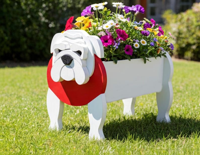 K&ouml;nnte beinhalten: Ein wei&szlig;er Holz-Bulldoggen-Pflanzk&uuml;bel mit rotem Kragen, gef&uuml;llt mit bunten Blumen. Der Pflanzk&uuml;bel ist wie eine Bulldogge geformt, mit Kopf und Beinen sichtbar. Die Blumen umfassen lila, wei&szlig;e, gelbe und rosa Bl&uuml;ten und bilden eine lebendige Darstellung.