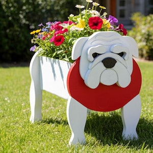 May include: A white wooden planter shaped like a bulldog, with a red collar and black nose. The planter is filled with colorful flowers, including red, yellow, and purple blooms. The planter is set on a green lawn.