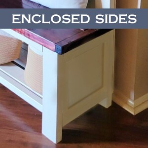 May include: A white bench with a dark wood top and enclosed sides. The bench has a shelf with woven baskets. The text "ENCLOSED SIDES" is displayed on a blue banner above the bench.