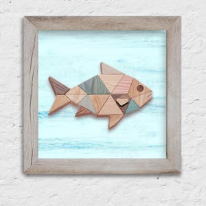 May include: Wooden fish art piece made of triangular blocks in shades of brown, pink, and blue. The fish is set against a light blue background with a wood-grain texture, framed in a light brown wooden frame.