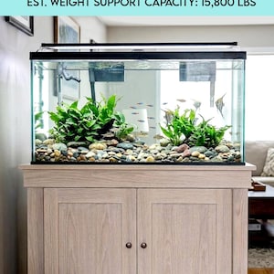 May include: A light-coloured solid wood aquarium stand supporting a glass fish tank filled with water, green aquatic plants, and river stones. Text at the top reads: 120 GALLON SOLID WOOD AQUARIUM STAND BUILDING INSTRUCTIONS EST. WEIGHT SUPPORT CAPACITY: 15,800 LBS.
