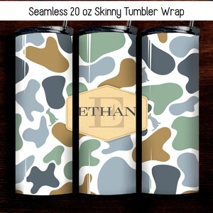 May include: A set of three 20 oz skinny tumblers with a camouflage pattern in shades of blue, green, and brown. One tumbler features a gold-colored label with the name "ETHAN". The tumblers have a black lid and a straw.