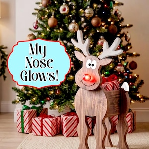 May include: A wooden reindeer figure with a glowing red nose and white antlers. The reindeer has a hollow body containing wrapped gifts. A light blue sign with a red border features the black text "My Nose Glows!" next to the figure.