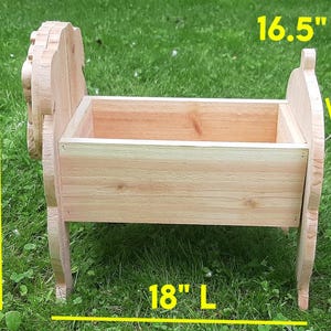 K&ouml;nnte beinhalten: Eine Holz-Pflanzkasten, 61 cm hoch, 42 cm breit und 46 cm lang. Der Pflanzkasten ist aus hellem Holz gefertigt und mit dekorativen Seitenteilen versehen. Er steht auf einer grasbewachsenen Oberfl&auml;che.