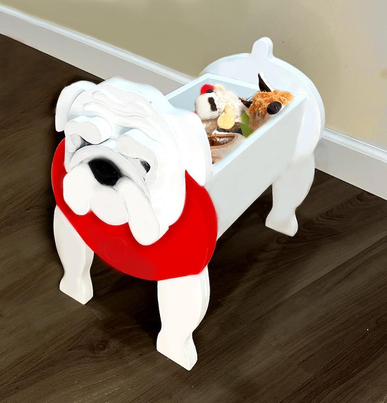 K&ouml;nnte beinhalten: Eine wei&szlig;e Holz-Aufbewahrungsbox in Form einer Bulldogge mit rotem Kragen. Die Box hat ein rechteckiges Staufach, das mit Stofftieren gef&uuml;llt ist. Die Bulldogge hat ein detailliertes Gesicht und steht auf vier Beinen.