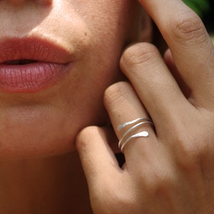 Könnte beinhalten: Ein silberner Ring mit einem einzigartigen, gedrehten Design. Der Ring wird am Zeigefinger einer Hand getragen.