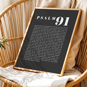 以下が含まれることがあります： 黒い背景に白い文字で「PSALM 91」と書かれた額入りのプリント。 プリントは金のフレームに入っており、籐の椅子に置かれた白いクッションの上にあります。 テキストは宗教的な一節です。