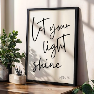 May include: A framed print with the words "Let your light shine" in black script. The print is set against a cream background and framed in black. The text "Matthew 5:16" is at the bottom right.