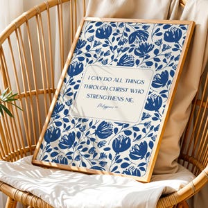 May include: A framed print featuring a floral pattern in navy blue on an off-white background. The print includes the text "I CAN DO ALL THINGS THROUGH CHRIST WHO STRENGTHENS ME." The frame is a light wood color, and the print is displayed on a wicker chair.