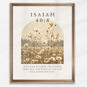 May include: Framed art print featuring a field of white flowers under a soft, arched design. The text "ISAIAH 40:8" is at the top, with the quote "THE GRASS WITHERS, THE FLOWER FADES, BUT THE WORD OF OUR GOD WILL STAND FOREVER" below.