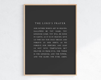 May include: A rectangular wall art print featuring the text of The Lord's Prayer in white serif font centered on a solid dark charcoal gray background, enclosed within a thin, light-toned wooden frame with a clean, simple border design.