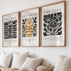 Puede incluir: Tres impresiones artísticas enmarcadas con diseños botánicos en negro y dorado. Las impresiones están etiquetadas como "THE WAY", "THE TRUTH" y "THE LIFE". Cada impresión tiene un marco de madera y se exhibe sobre un banco con almohadas.
