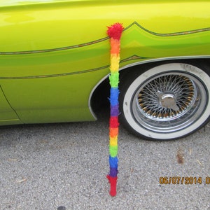 Puede incluir: Un coche amarillo brillante con un neumático de banda blanca y una piñata de arcoíris colgando del lateral.