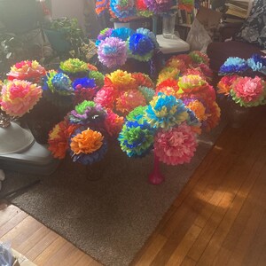 Puede incluir: Una colecci&oacute;n de ramos de flores de papel de colores en varios tonos de azul, verde, amarillo, naranja y rosa. Los ramos est&aacute;n dispuestos en un suelo de madera con una alfombra marr&oacute;n.