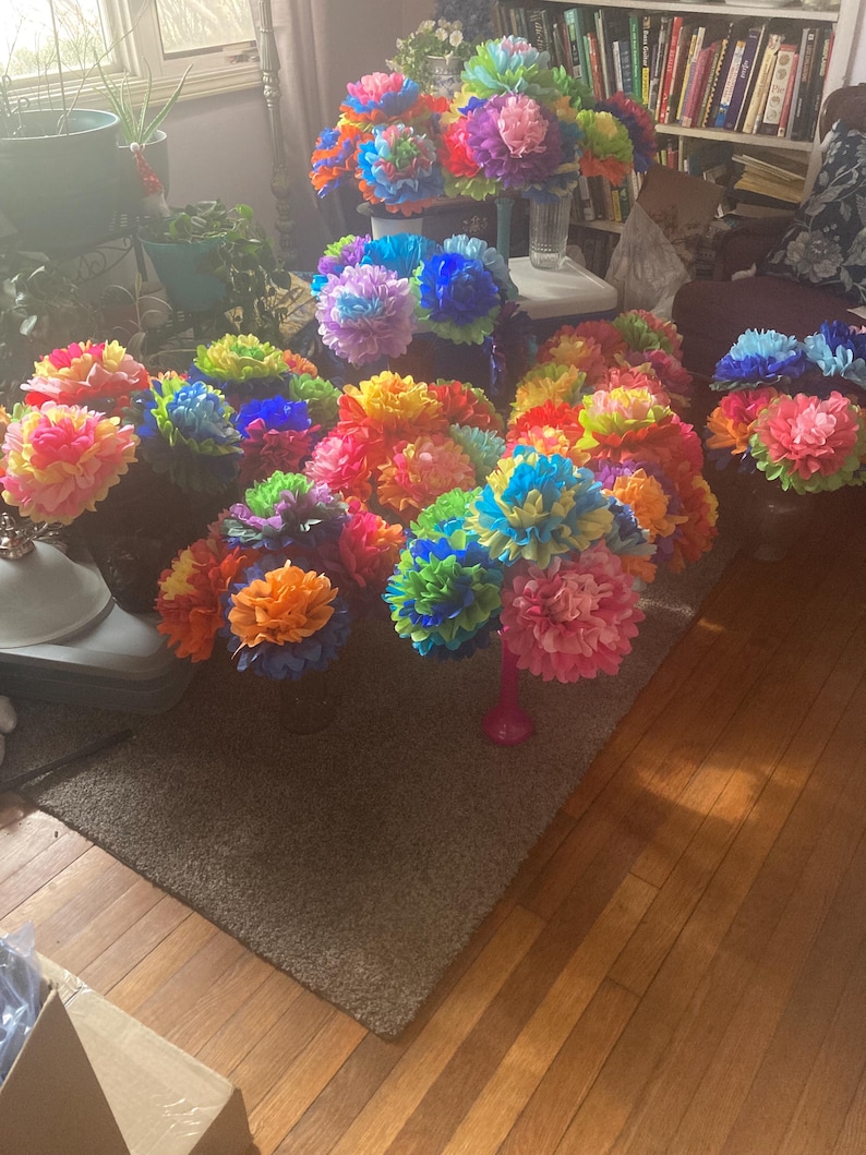 Puede incluir: Una colecci&oacute;n de ramos de flores de papel de colores en varios tonos de azul, verde, amarillo, naranja y rosa. Los ramos est&aacute;n dispuestos en un suelo de madera con una alfombra marr&oacute;n.