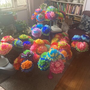 Puede incluir: Una colecci&oacute;n de ramos de flores de papel de colores en varios tonos de azul, rosa, amarillo, naranja y verde. Los ramos est&aacute;n dispuestos en un suelo de madera y una alfombra.