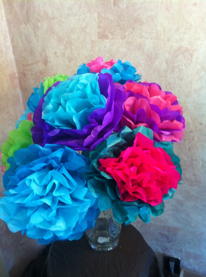 Puede incluir: Un ramo de flores de papel de seda de colores en tonos azules, morados, rosas y verdes. Las flores est&aacute;n dispuestas en un jarr&oacute;n de vidrio transparente.