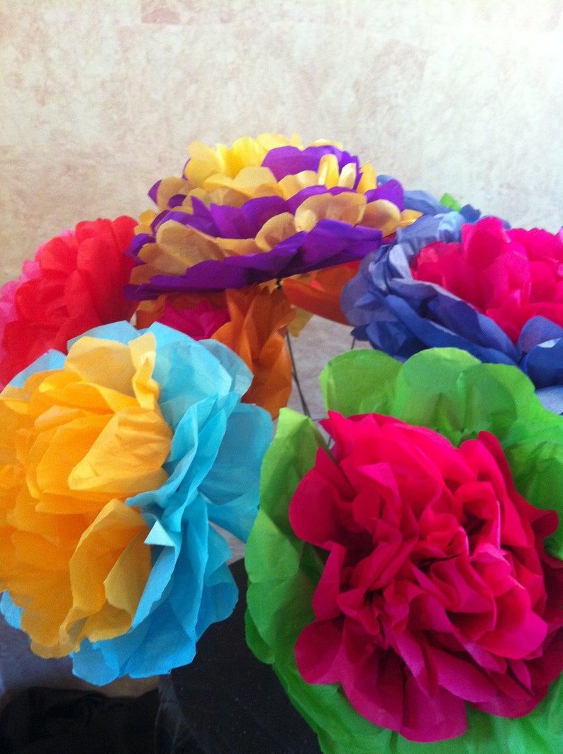 Puede incluir: Un ramo de flores de papel de seda de colores en tonos de azul, amarillo, naranja, rosa y verde. Las flores est&aacute;n dispuestas en forma circular y est&aacute;n hechas para parecer claveles.