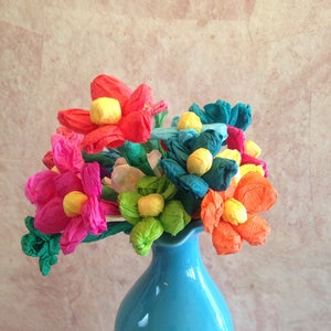 Puede incluir: Un ramo de flores de papel de seda de colores en un jarrón azul claro. Las flores son rosas, rojas, naranjas, verdes y azules.