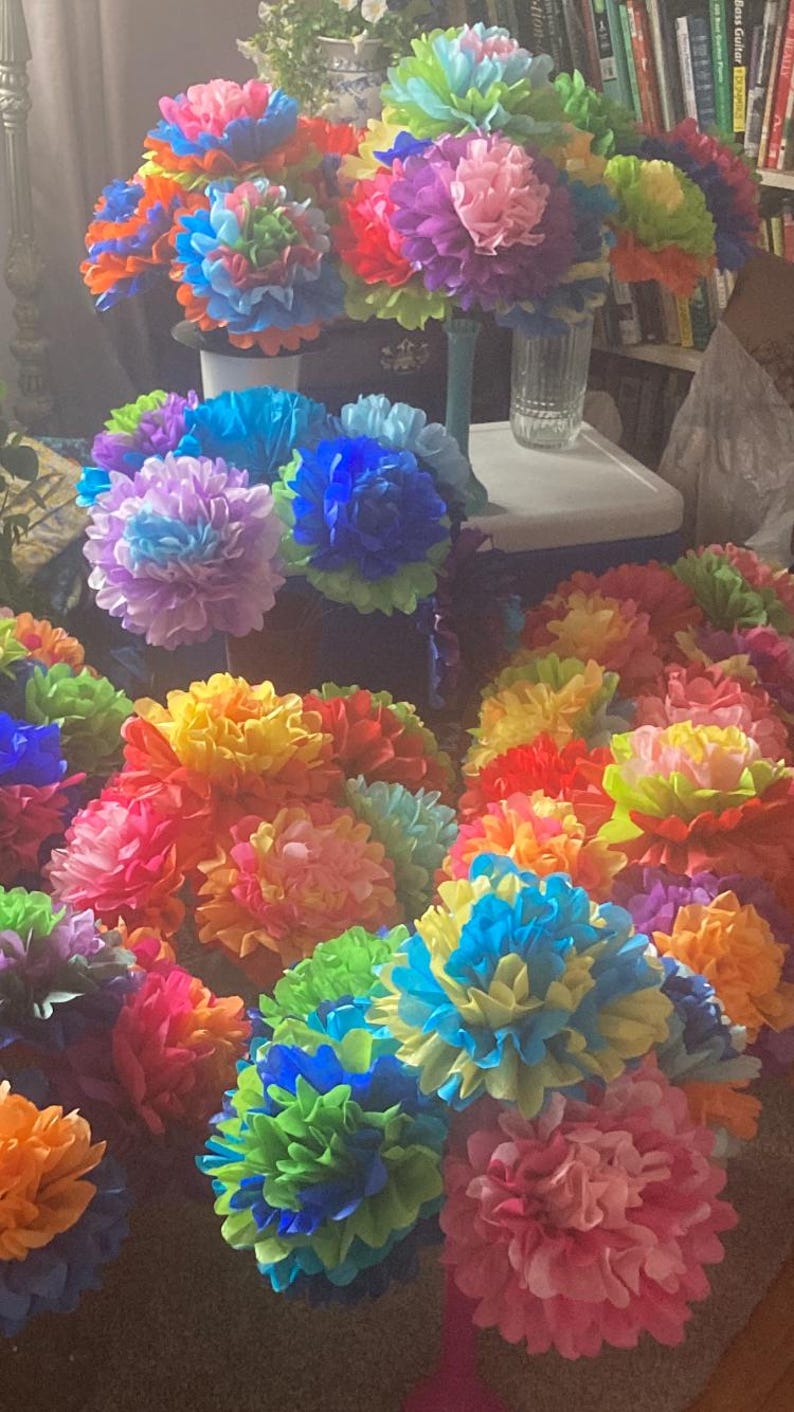 Puede incluir: Una colecci&oacute;n de pompones de papel de seda coloridos en varios tonos de azul, verde, rosa, amarillo y naranja. Los pompones est&aacute;n dispuestos en una exhibici&oacute;n decorativa, creando un ambiente vibrante y festivo.