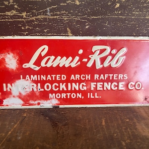 May include: Vintage red and white metal sign for "Lami-Rib" with the text "Laminated Arch Rafters" and "Interlocking Fence Co., Morton, Ill." The sign has a distressed appearance.