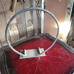 May include: A silver metal hoop with a flat base, mounted on a red table with gold accents.