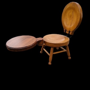 May include: A wooden stool with a round seat and a hinged lid that opens to reveal a circular tray. The stool is made of light brown wood and has a simple design.