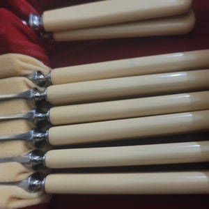 May include: Set of eight silver-plated butter knives with ivory-colored handles. The knives are arranged in a row, with the handles facing up.