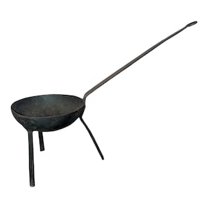 May include: A black, cast iron cooking ladle with a long handle and three legs. The ladle has a round bowl and is designed for use over an open fire. The handle extends at an angle from the bowl, providing a comfortable grip for stirring and serving.